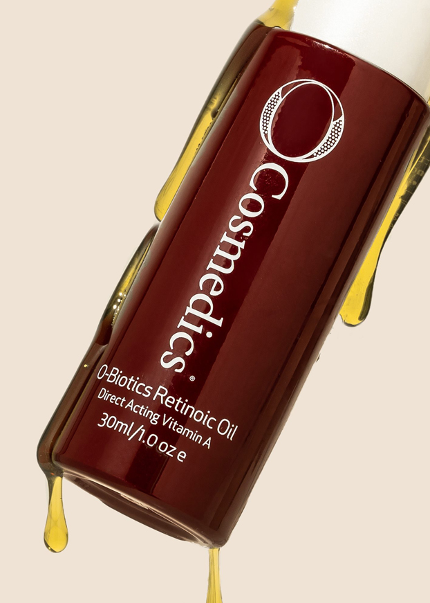A bottle of O Cosmedics Retinoic Oil dripping in oil.