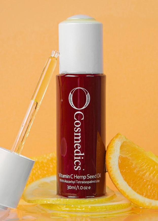 A bottle of O Cosmedics Vitamin C Hemp Seed Oil serum standing next to slices of oranges to represent the high amount of vitamin C content in the ingredients. 
